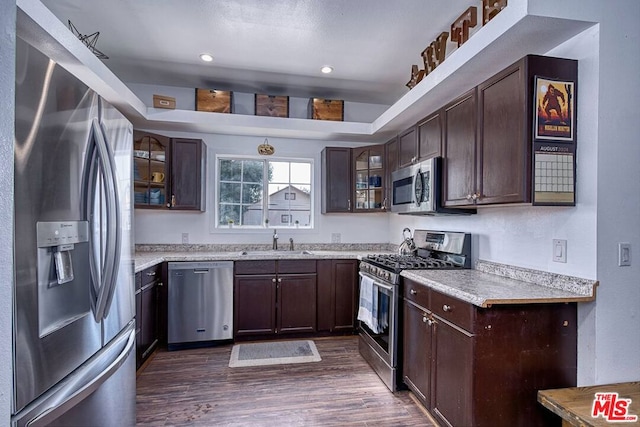 kitchen with light stone counters, appliances with stainless steel finishes, dark hardwood / wood-style floors, dark brown cabinetry, and sink