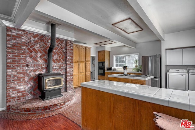 kitchen featuring washing machine and clothes dryer, beamed ceiling, black appliances, light hardwood / wood-style floors, and tile counters