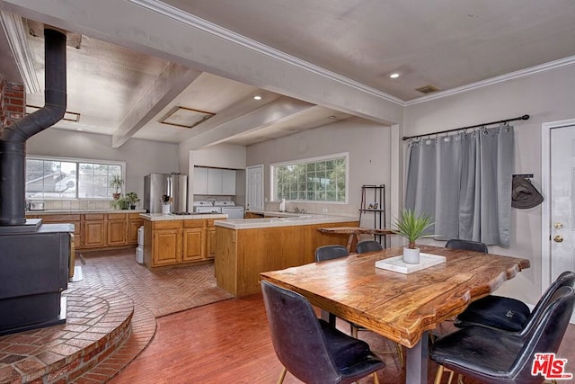 dining space featuring washer / clothes dryer, a wood stove, beam ceiling, ornamental molding, and light hardwood / wood-style flooring