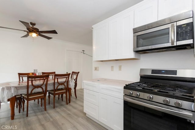 kitchen with light wood-type flooring, stainless steel appliances, ornamental molding, and white cabinetry