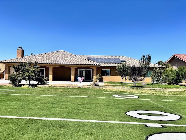 view of front of home with a patio, a front yard, and solar panels