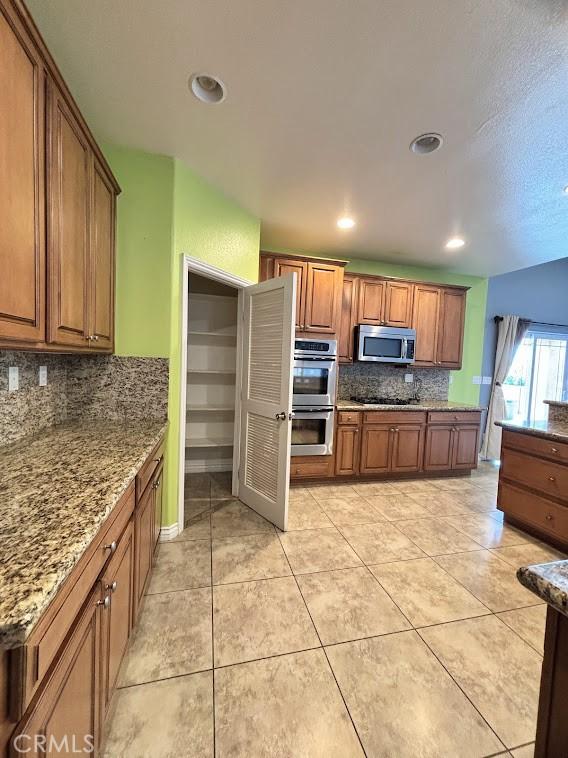 kitchen with tasteful backsplash, stone counters, light tile patterned floors, and stainless steel appliances