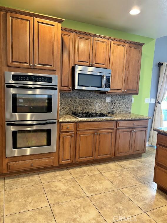 kitchen featuring light tile patterned floors, light stone countertops, backsplash, and appliances with stainless steel finishes