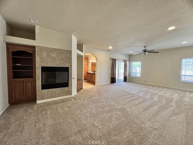 unfurnished living room with a tile fireplace, light colored carpet, a healthy amount of sunlight, and a textured ceiling