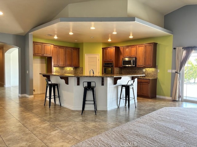 kitchen with lofted ceiling, a spacious island, decorative backsplash, appliances with stainless steel finishes, and a kitchen bar