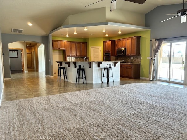 kitchen featuring backsplash, a spacious island, vaulted ceiling, a kitchen bar, and appliances with stainless steel finishes