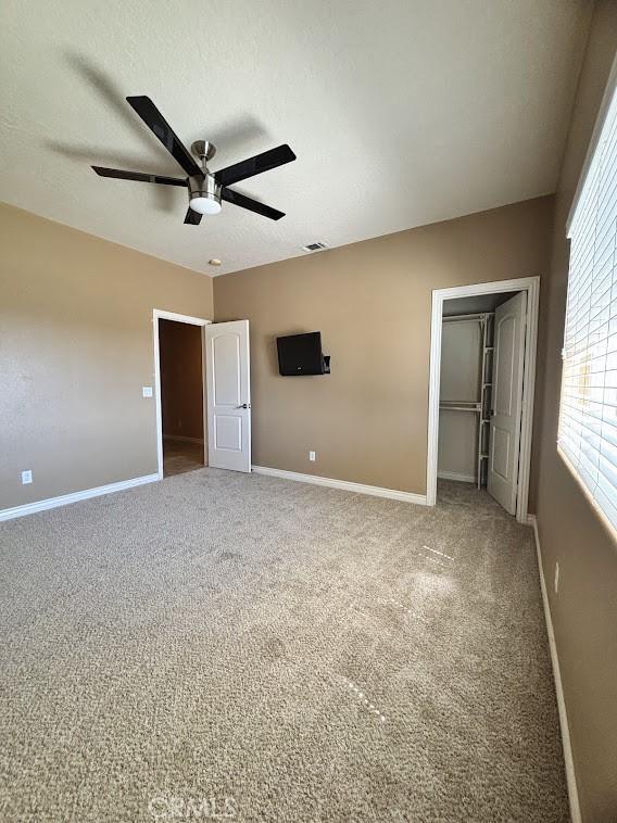 unfurnished bedroom with carpet, a closet, a spacious closet, and ceiling fan