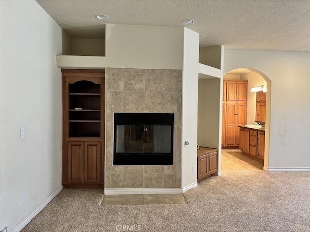 unfurnished living room with a textured ceiling, built in shelves, light carpet, and a tiled fireplace