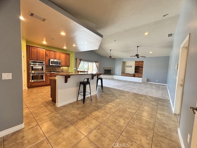 kitchen featuring ceiling fan, dark stone counters, a breakfast bar area, light tile patterned floors, and appliances with stainless steel finishes