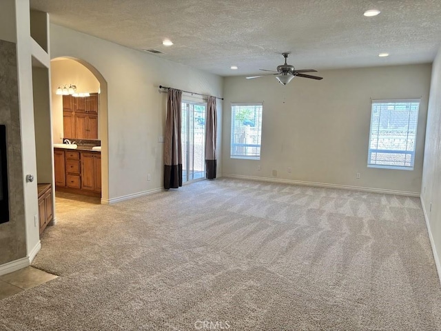 unfurnished room featuring a wealth of natural light, ceiling fan, light carpet, and a textured ceiling