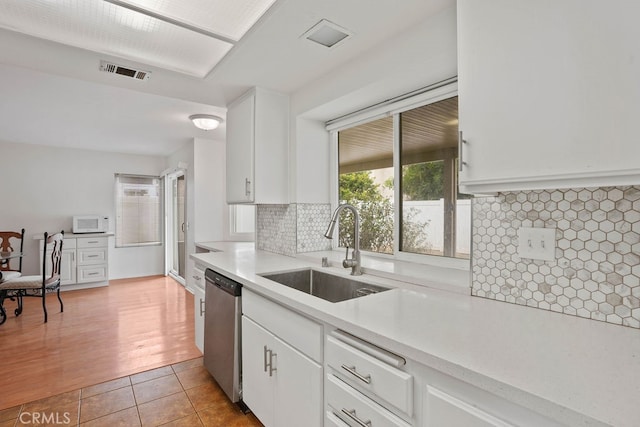 kitchen with decorative backsplash, light hardwood / wood-style floors, white cabinets, stainless steel dishwasher, and sink