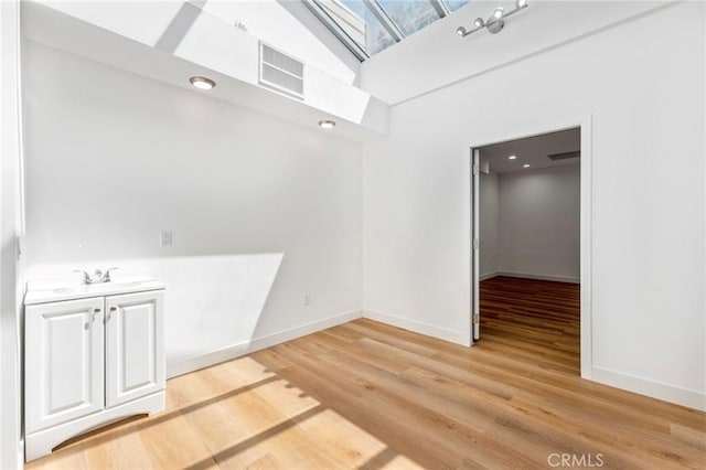 unfurnished room with sink, light wood-type flooring, and a towering ceiling