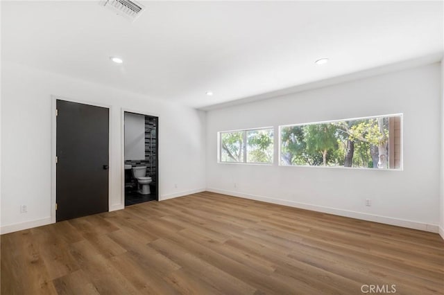 unfurnished bedroom featuring hardwood / wood-style flooring, ensuite bathroom, and multiple windows