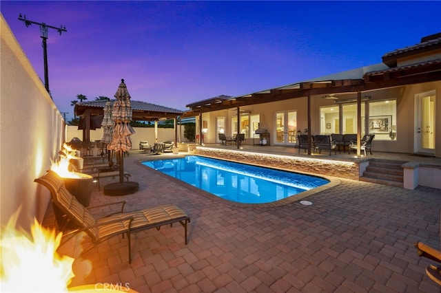 pool at dusk featuring a patio, a gazebo, and an outdoor living space with a fireplace