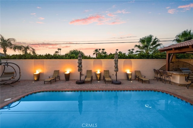 pool at dusk featuring a patio area and a bar