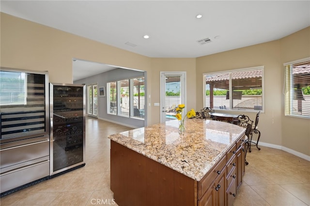 kitchen featuring a kitchen island, light stone countertops, light tile patterned floors, and beverage cooler