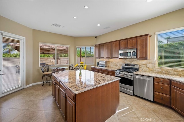 kitchen with a center island, light stone countertops, stainless steel appliances, and a wealth of natural light