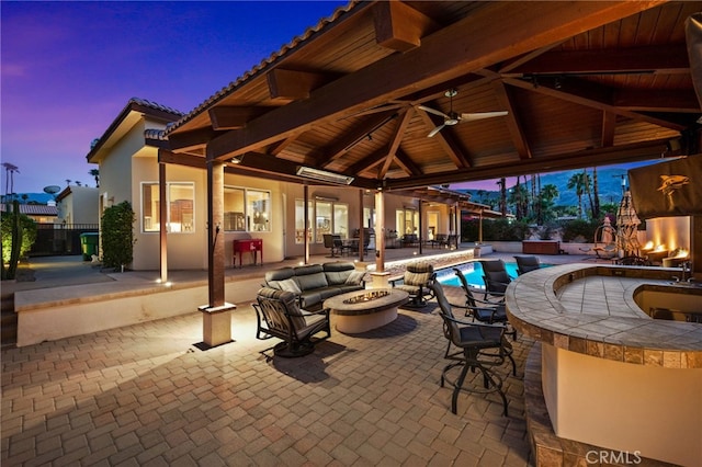 patio terrace at dusk with an outdoor fire pit, a gazebo, an outdoor bar, and ceiling fan