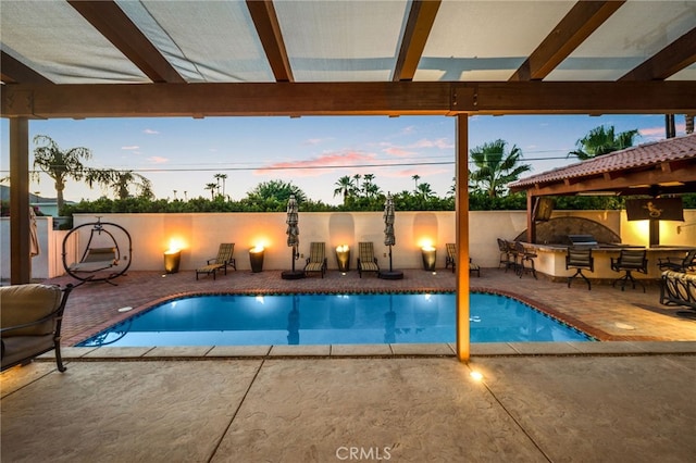 pool at dusk featuring a patio, exterior bar, and exterior kitchen