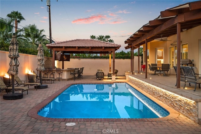 pool at dusk with a bar, a gazebo, and a patio area