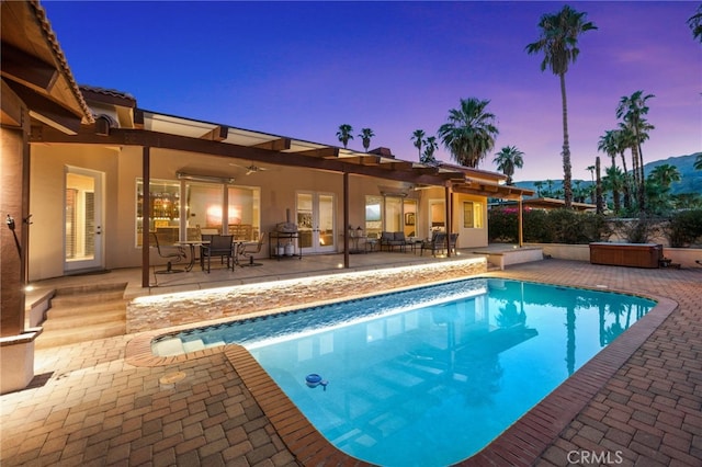 pool at dusk featuring a patio area, a jacuzzi, and ceiling fan