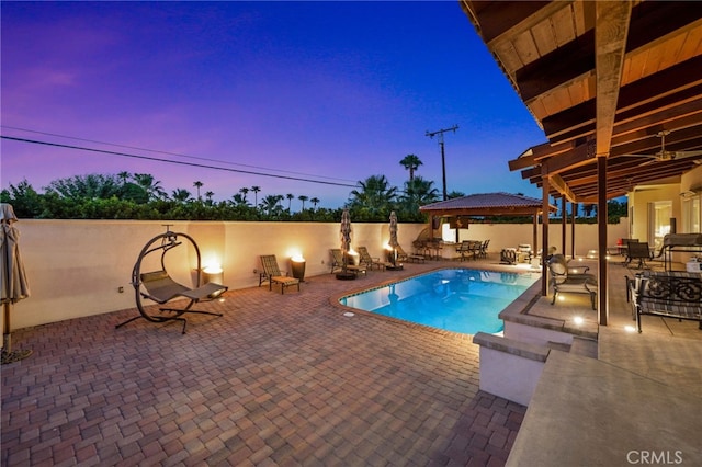 pool at dusk featuring a gazebo and a patio