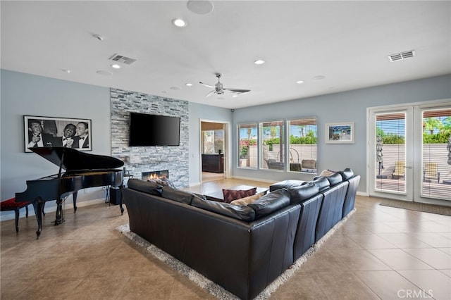 tiled living room featuring a stone fireplace and ceiling fan