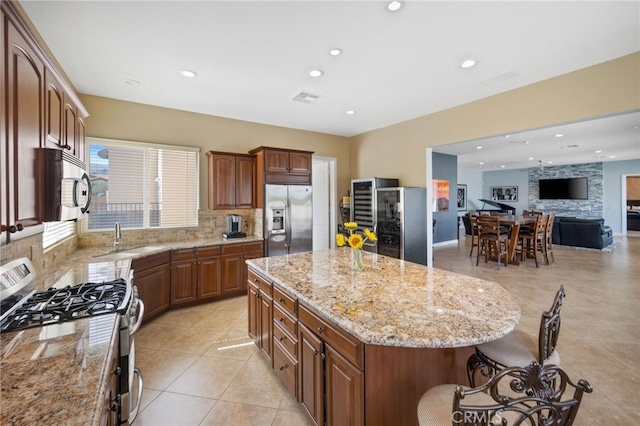 kitchen with sink, a center island, light tile patterned floors, appliances with stainless steel finishes, and light stone counters