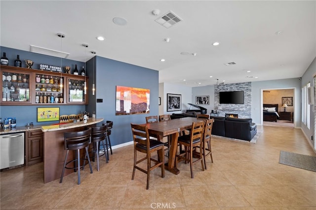 tiled dining space featuring a stone fireplace and indoor bar