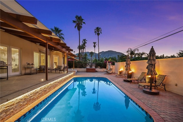 pool at dusk featuring a patio and a mountain view