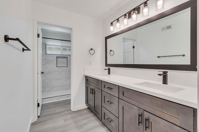 bathroom featuring a tile shower, double vanity, and hardwood / wood-style floors