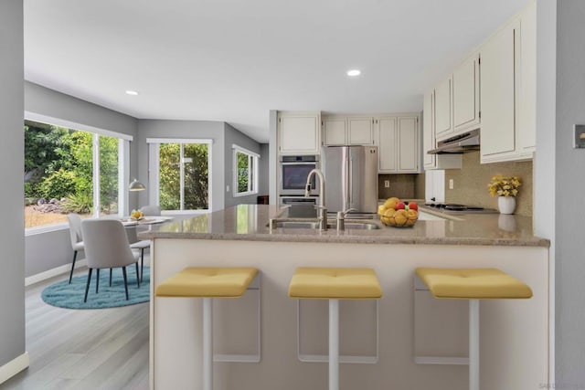 kitchen with appliances with stainless steel finishes, backsplash, kitchen peninsula, and light hardwood / wood-style floors