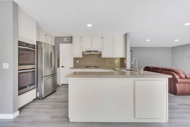 kitchen featuring decorative backsplash, appliances with stainless steel finishes, white cabinets, light wood-type flooring, and kitchen peninsula