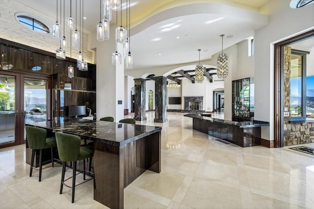 kitchen with a kitchen bar, decorative light fixtures, a stone fireplace, and dark brown cabinetry