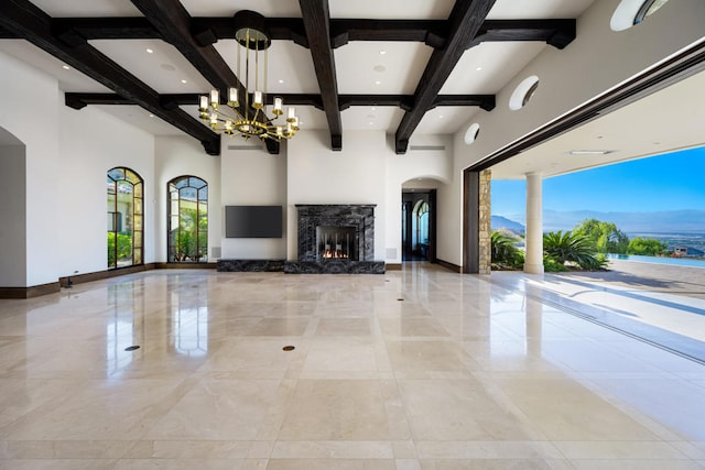 unfurnished living room with beam ceiling, a high ceiling, a premium fireplace, a mountain view, and a chandelier