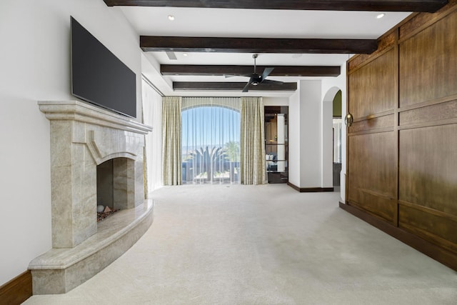 unfurnished living room featuring a fireplace, beam ceiling, light colored carpet, and ceiling fan