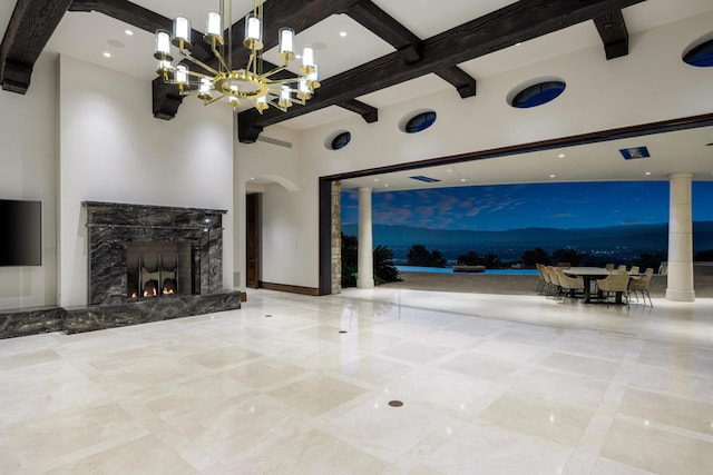 unfurnished living room featuring a fireplace, beamed ceiling, a high ceiling, and a notable chandelier