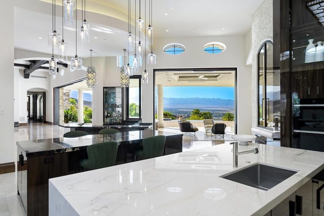 kitchen featuring pendant lighting, a mountain view, a large island with sink, light stone countertops, and light tile patterned flooring