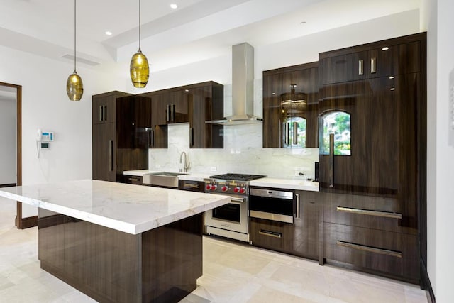 kitchen featuring decorative backsplash, stainless steel appliances, sink, wall chimney range hood, and decorative light fixtures