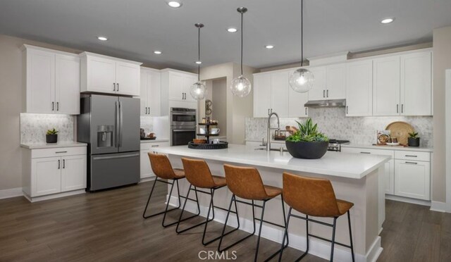 kitchen featuring white cabinets, an island with sink, decorative light fixtures, dark wood-type flooring, and appliances with stainless steel finishes