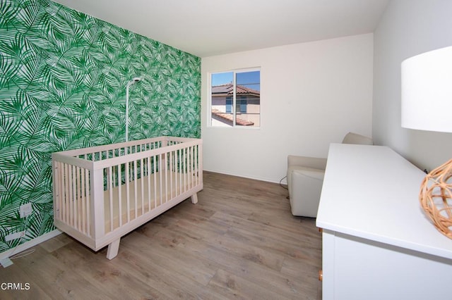 bedroom with wood-type flooring and a nursery area