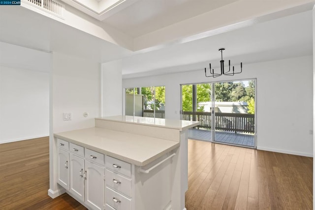 kitchen with kitchen peninsula, hardwood / wood-style flooring, hanging light fixtures, a notable chandelier, and white cabinetry