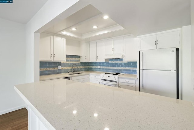 kitchen featuring white appliances, light stone countertops, a tray ceiling, sink, and white cabinetry