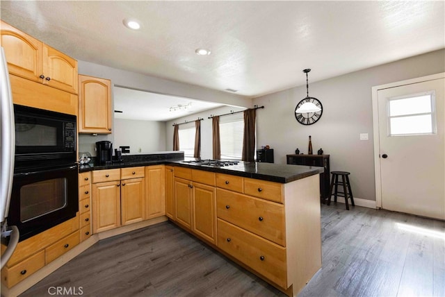 kitchen with kitchen peninsula, hanging light fixtures, black appliances, light brown cabinets, and dark hardwood / wood-style flooring