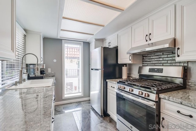 kitchen with light stone counters, gas range, white cabinets, sink, and backsplash