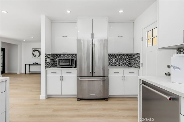 kitchen with white cabinets, backsplash, light hardwood / wood-style floors, and appliances with stainless steel finishes