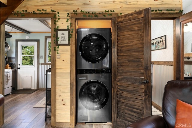 washroom featuring wood-type flooring, wood walls, and stacked washing maching and dryer