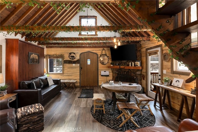 living room with a healthy amount of sunlight, a stone fireplace, wood walls, and dark wood-type flooring