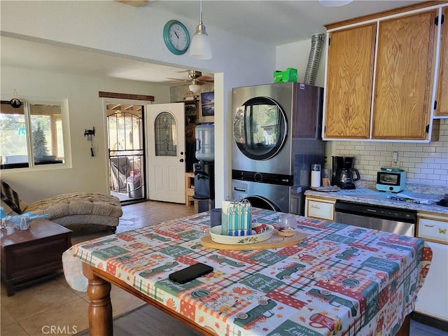 kitchen with backsplash, stainless steel dishwasher, ceiling fan, dark tile patterned floors, and stacked washing maching and dryer