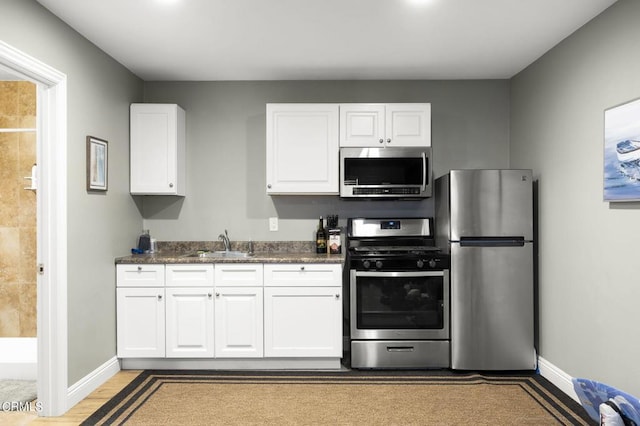 kitchen with sink, dark stone countertops, light wood-type flooring, white cabinetry, and stainless steel appliances